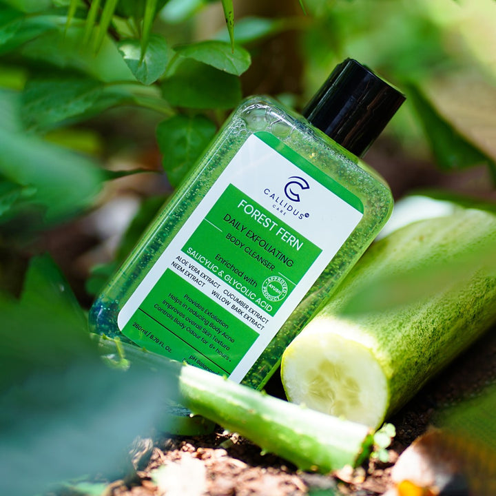 Forest Fern Body Cleanser lying on the soil next to sliced cucumber and aloe leaves, surrounded by natural greenery.